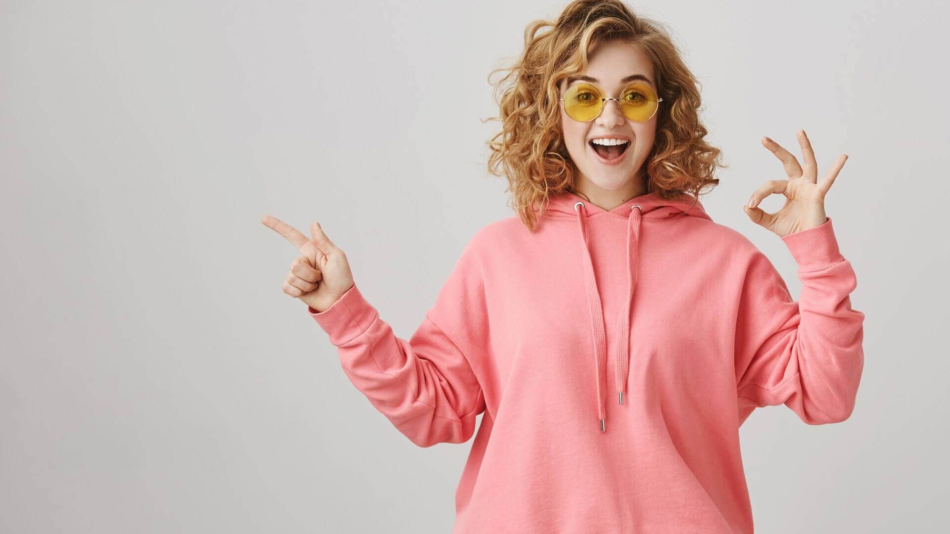 Person wearing a pink hoodie and yellow sunglasses on a plain background